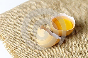 Close up broken raw egg with the yolk and albumen on a linen tablecloth on white background