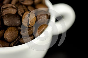 Close up of brown coffee beans in a white mug.