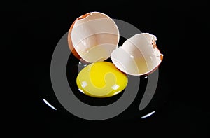 Close up of brown cracked egg shell with raw yellow yalk and slimy egg white on reflecting shiny black background