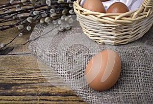 Close up brown egg, basket, burlap, willow twigs on wooden background