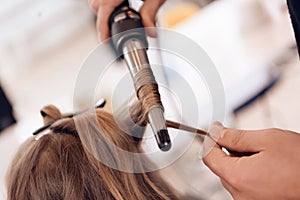 Close up. Brown hair woman does curling hair in beauty salon. Hairdresser make hair wave for woman.