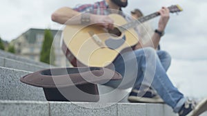 Close-up of brown hat on urban stairs with blurred man playing guitar at the background. Unrecognizable Caucasian