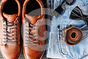 Close up of brown leather men`s boots, belt, sunglasses and blue jeans top view