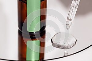 Close up of brown serum or oil glass with green stiker mock up on bottle on mirror background. Drops of liquid in a pipette