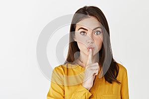 Close-up of brunette woman hushing, tell be quiet, share a secret and looking at camera, showing taboo sign while