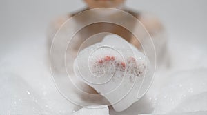 Close-up bubble foam on boy hands surrounded by soap suds when taking a bath in bathtub. Funny, healthcare lifestyle and hygiene