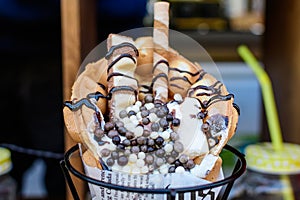 Close up of a bubble waffle with marshmallow, chocolate syrup, wafer and cream in display at a street food market, selective focus