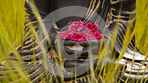 Close up of buddha figurine with red flowers in the middle of green meadow