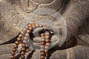 Close up on a Buddha statue hands holding a wooden prayer beads rosary