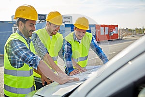 Close up of builders with blueprint on car hood