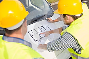 Close up of builders with blueprint on car hood