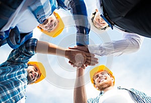 Close up of builders in hardhats with hands on top