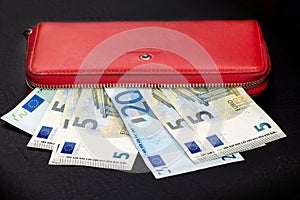 Close up of bundles of euro banknotes and opening a red wallet on a dark background. Selective focus