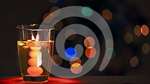Close up. Burning Christmas candle in a transparent glass beaker. Multicolored circles on a black background