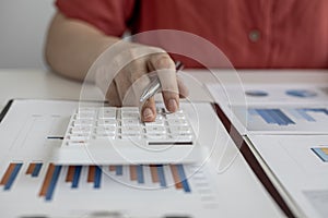 A close-up of a business finance woman`s hand pressing a white calculator to calculate numbers from company financial documents.