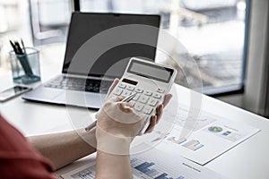 A close-up of a business finance woman`s hand pressing a white calculator to calculate numbers from company financial documents.