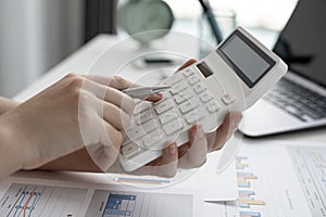 A close-up of a business finance woman`s hand pressing a white calculator to calculate numbers from company financial documents.