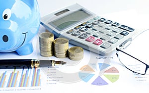 Close up of business fountain pen with money coins stack with calculator and eyeglasses and blue piggy bank with document chart