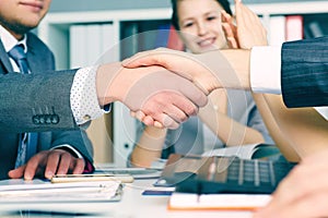 Close up business handshake on team meeting with clapping group of people blured in background at modern startup