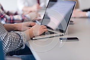 close up of business man hands typing on laptop with team on meeting in background