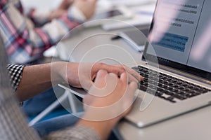 close up of business man hands typing on laptop with team on meeting in background