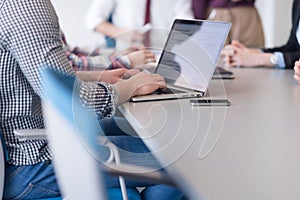 close up of business man hands typing on laptop with team on meeting in background