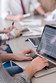 close up of business man hands typing on laptop with team on meeting in background