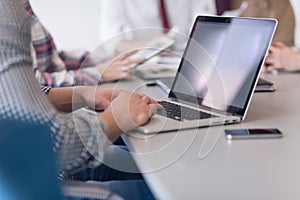 close up of business man hands typing on laptop with team on meeting in background