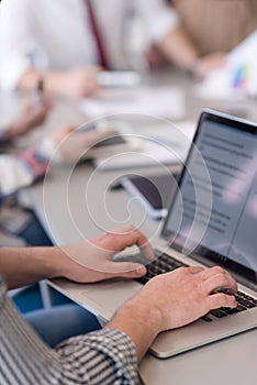 close up of business man hands typing on laptop with team on meeting in background