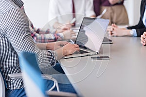 close up of business man hands typing on laptop with team on meeting in background