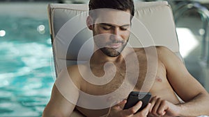 Closeup man looking phone by pool. Male relaxing with phone at wellness center