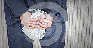 Close up of business man`s hands behind back with money and handcuffs against grey wood panel