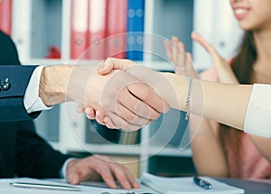 Close up business people handshake on team meeting with clapping group of people blured in background at modern startup