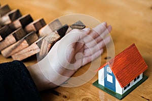 Close-up Of Business Woman Hand Stopping and Covering The Wooden Blocks From Falling On House Model, insurance concept