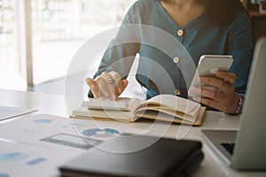 Close up business woman hand using mobile smartphone and calculator, work on laptop computer with calculator on the desk