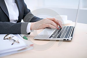 Close-up of business woman hands typing on laptop computer in the white colored office.