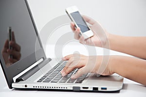 Close Up Business Woman's hand typing on a laptop keyboard with a mobile phone