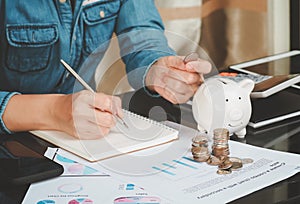 Close up of business woman`s hands writing on a paper on the table hand holding coin and stack coins working calculating monthly