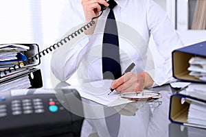 Close up of business woman talking by phone while making report, calculating or checking balance.