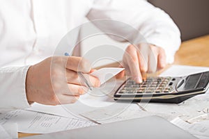 Close up of businessman or accountant hand holding pen working on calculator accountancy document and laptop computer at office,