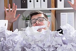 Close-up Of Businessman Behind Heap Of Crumpled Paper