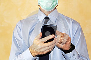 Close-up - businessman in a blue shirt and protective medical mask holds a smartphone in his hand