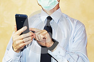 Close-up - businessman in a blue shirt and protective medical mask holds a smartphone in his hand