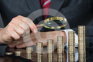 Close-up Of Businessman Examining Coins With Magnifier
