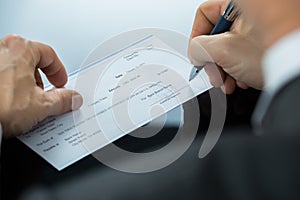 Close Up Of Businessman Filling Blank Cheque At Desk