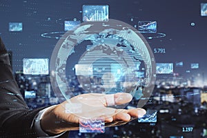 Close up of businessman hand holding abstract globe with forex charts and graphs on blurry night city background. Global trading