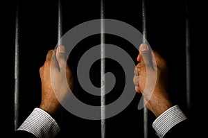 Close-up Of Businessman Hand Holding Metal Bars In Jail with dark environments
