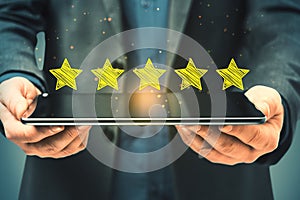 Close up of businessman hand holding tablet with 5 star rating on blurry background. Customer service and excellent feedback
