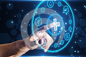Close up of businessman hand pointing at creative round medical interface with cross and other icons on blue background.