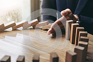 Close up of businessman hand Stopping Falling wooden Dominoes effect from continuous toppled or risk, strategy and successful int